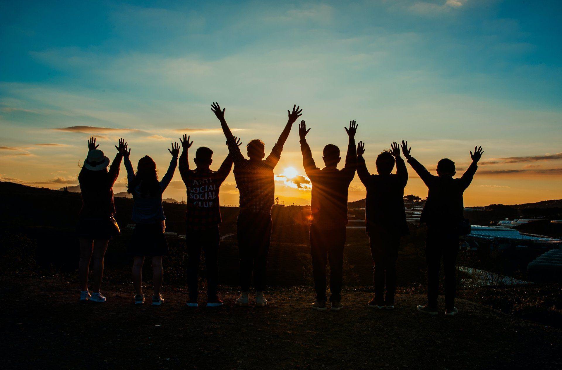 Silhouettes of a group raising their arms at sunrise